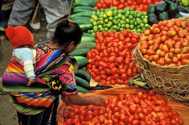 Woman carrying a child on her back at Gaute market surrounded by produce