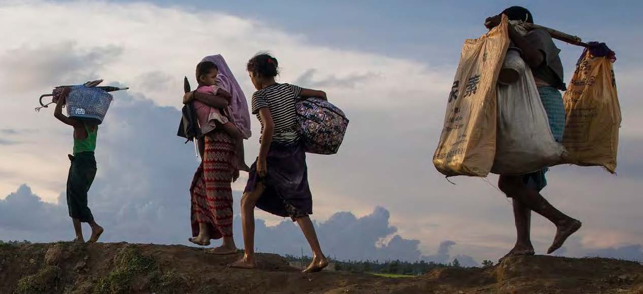 Four people carrying bundles and a child across open land.