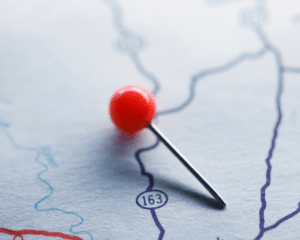 A red push pin resting on generic road map