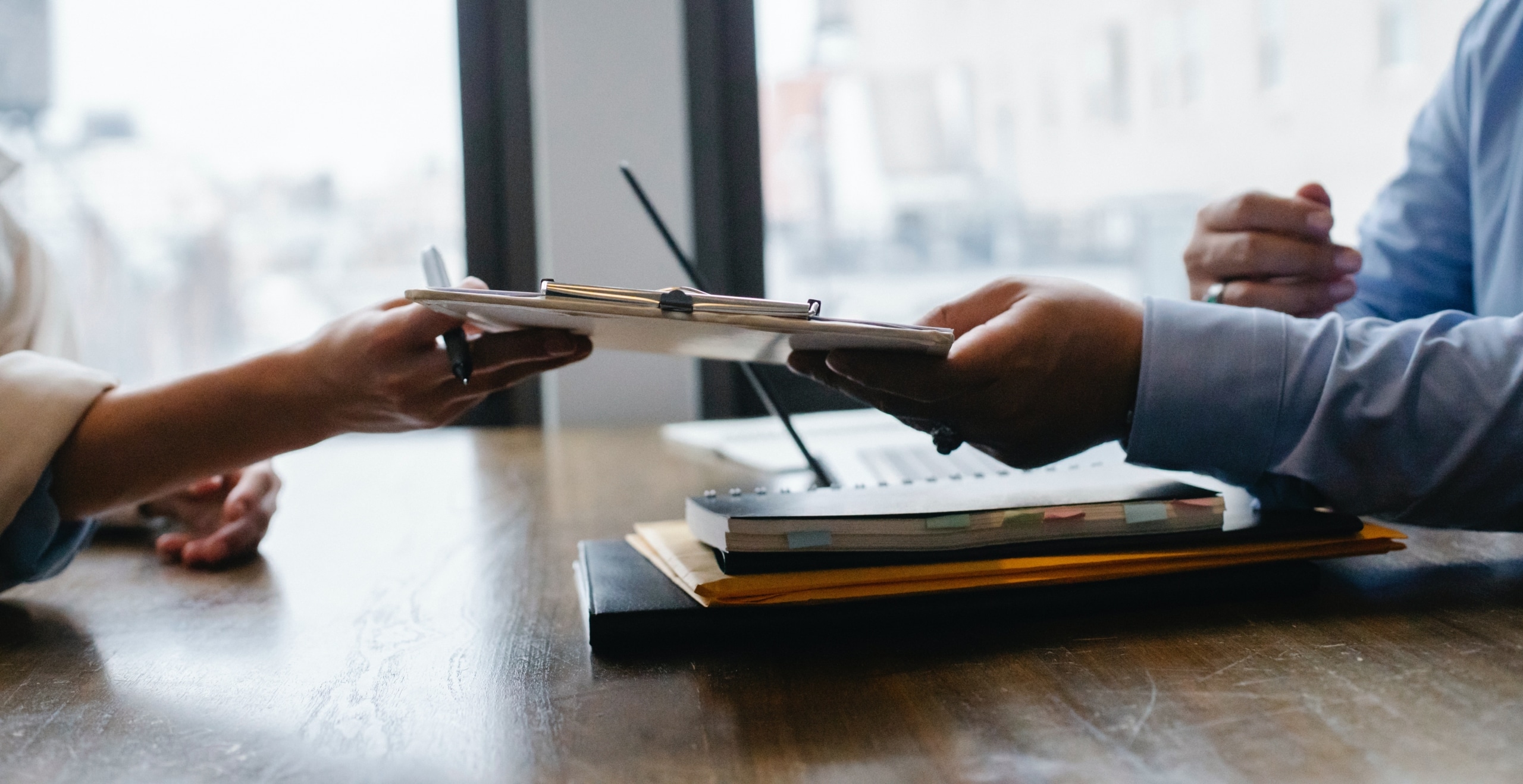 Person handing another person a clipboard with a form and pen