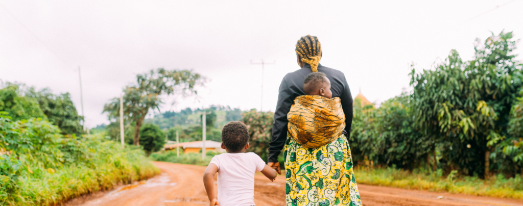 African Mother And Two Children Walk Alone In Red Clay Road In Village 